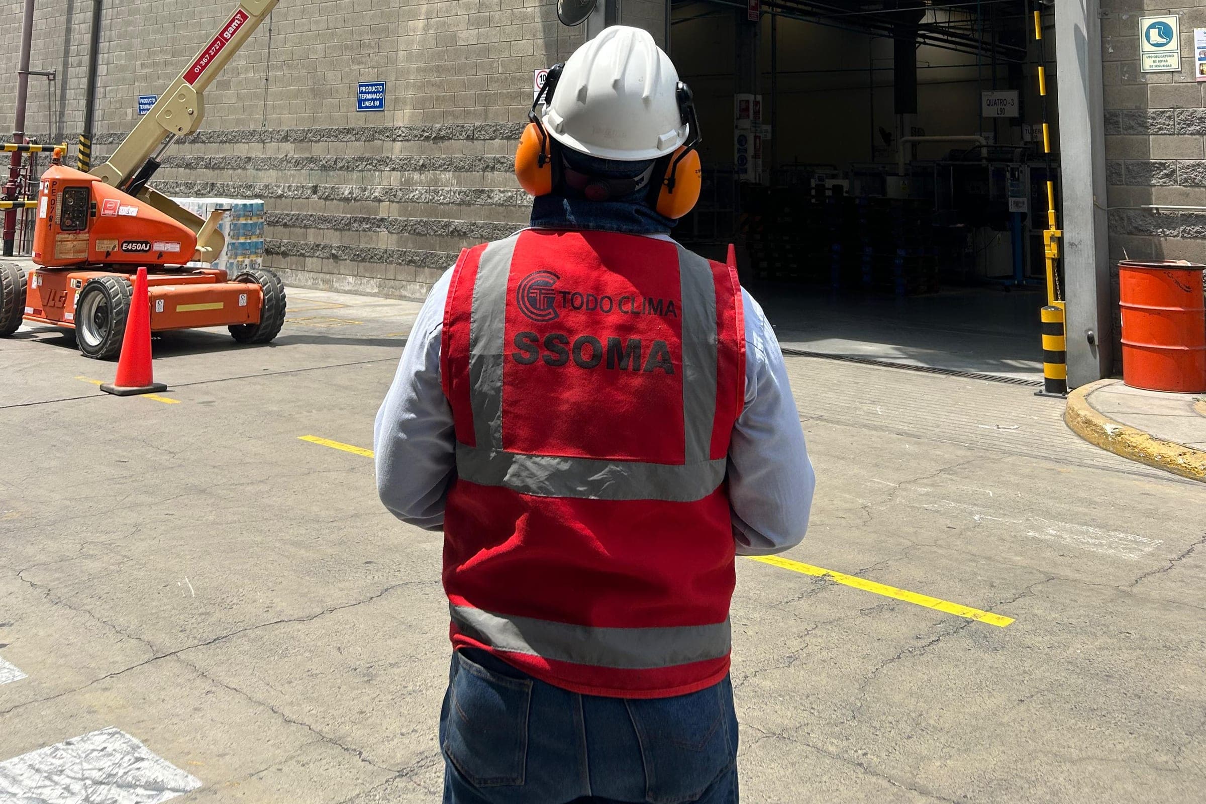 Supervisor de seguridad de Grupo TodoClima, con casco y chaleco SSOMA, vigilando el montaje de equipos desde una plataforma elevadora en una planta industrial.